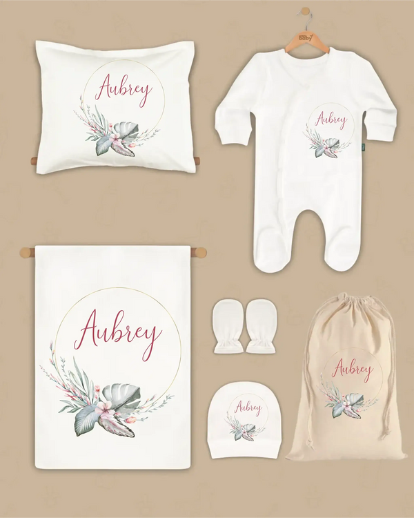 Gepersonaliseerde newborn 6-delige set met naam en bloemenaccenten, inclusief dekentje, kussen, boxpakje, hoed en tas.