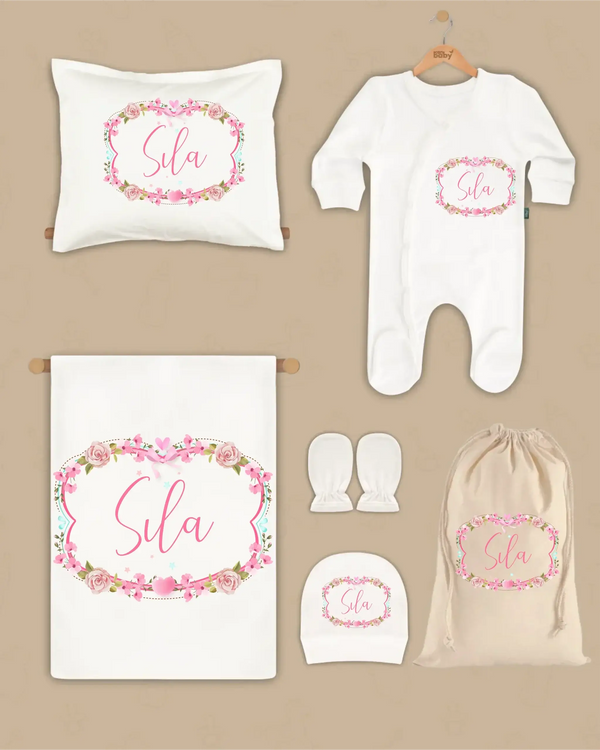 Gepersonaliseerde 6-delige newborn cadeauset met roze bloemen, naam Sila, inclusief dekentje, kussen, boxpakje, en hoed.