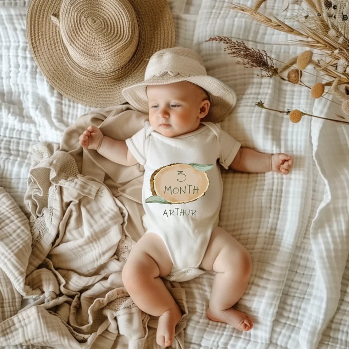 Baby in a hat wearing a personalized 3 Month milestone romper with name Arthur, on a cozy blanket.