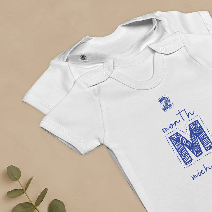 Gepersonaliseerde baby rompers in wit met maandmarkeringen voor mijlpalen en naam, perfect voor elke ouder.