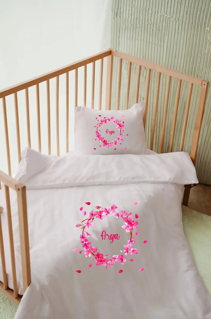 Roze gepersonaliseerd dekbedovertrek met naam in wieg, met bloemenprint en bijpassende kussensloop.