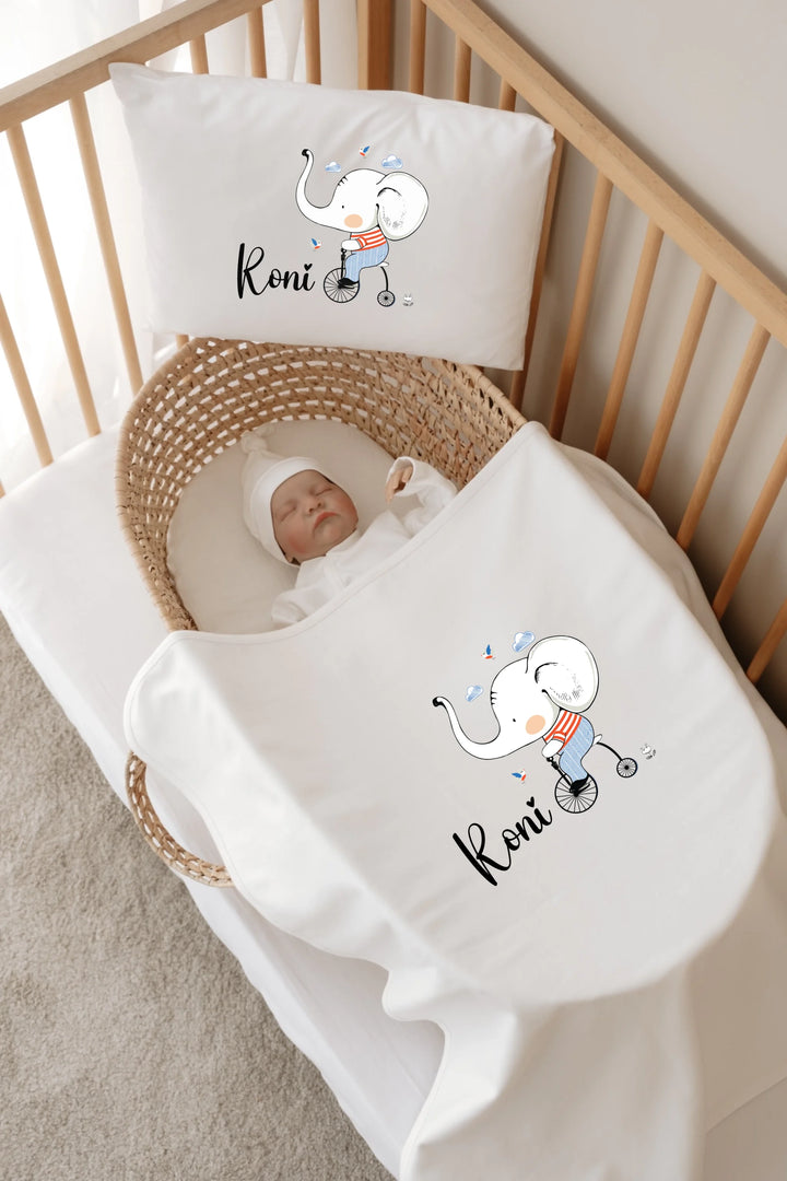 Babykamer met olifant beddengoed en naam, schattige baby ligt in een mandje met wit dekentje.