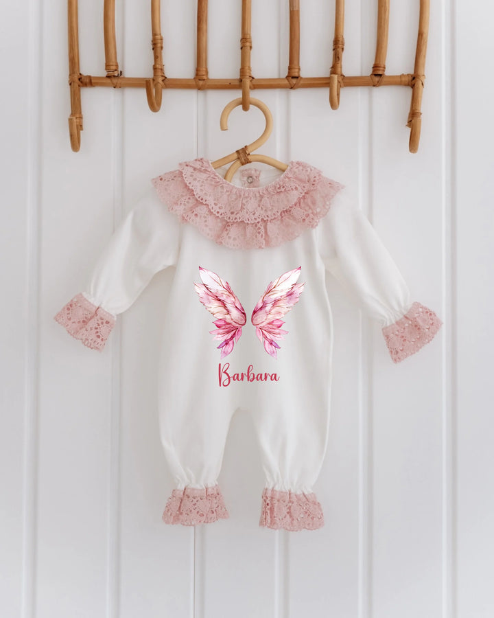 Gepersonaliseerd kanten babypakje met roze vleugels en naam voor meisjes, ideaal als kraamcadeau.
