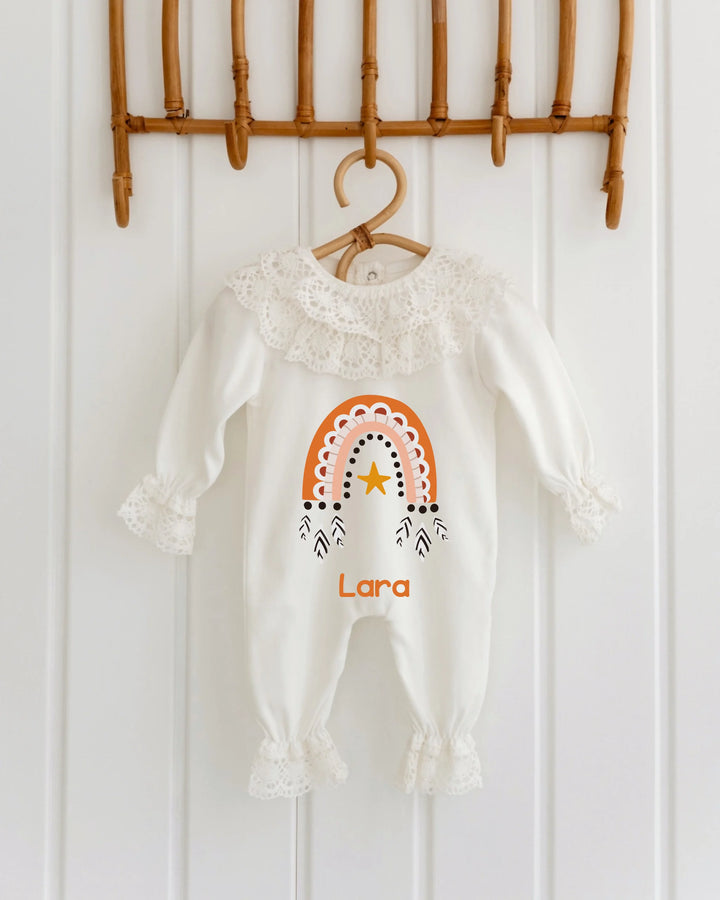 Kanten babypakje met regenboogdesign en de naam Lara in terracotta en oranje tinten.