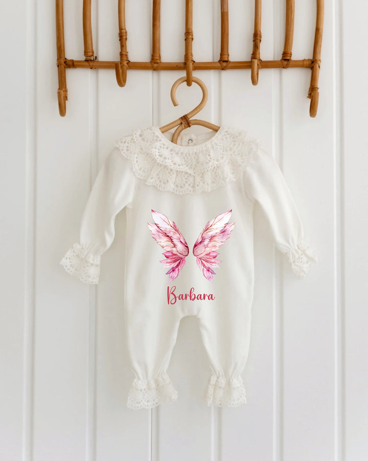Gepersonaliseerd kanten babypakje met roze vleugels en naam, ideaal als geboortepakje of kraamcadeau.