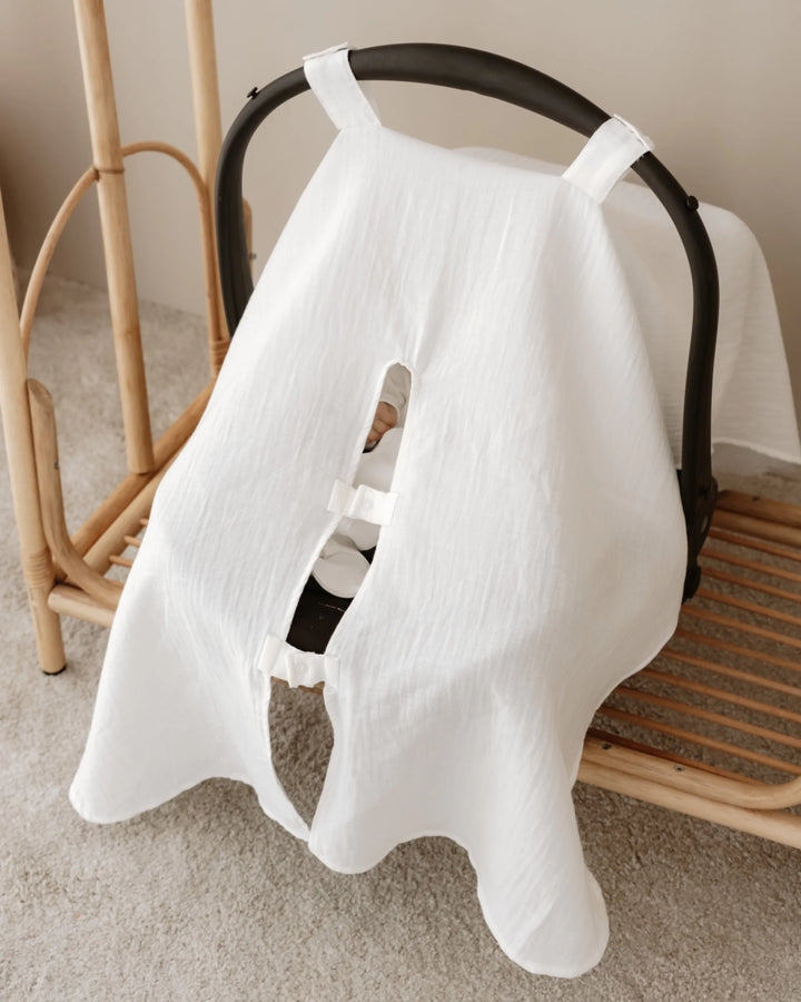 Zachte, witte zonnekap voor autostoel 0+ met openingen voor veiligheidsgordels, perfect voor baby's comfort.