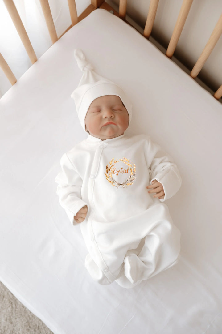 Babypop in een witte outfit met naam en een puntmuts, liggend in een babybedje.