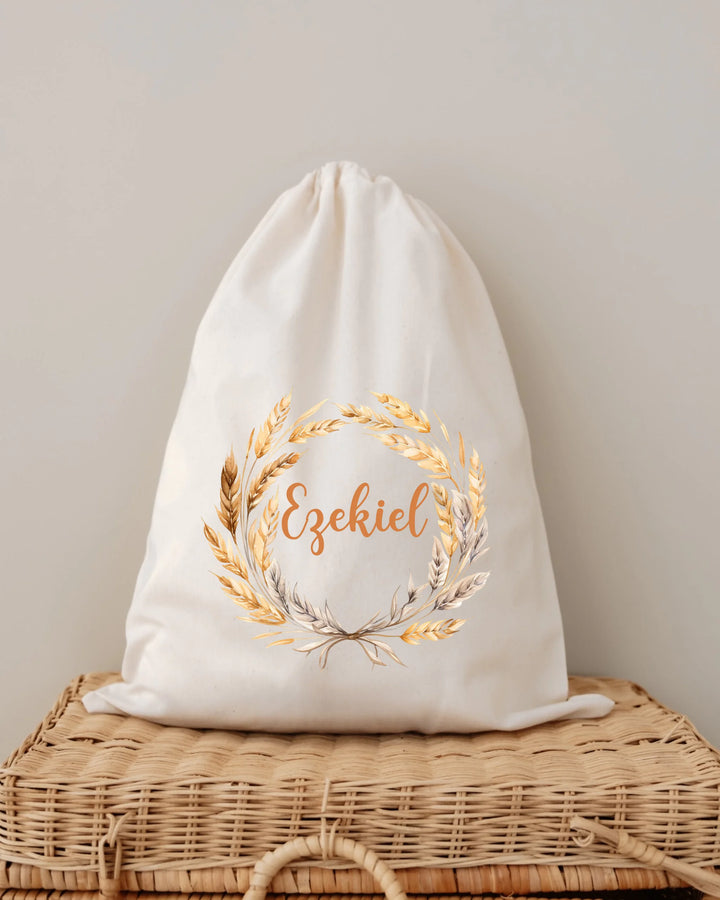 Gepersonaliseerde newborn tas met de naam Ezekiel en gouden tarwekrans op een natuurlijke achtergrond.
