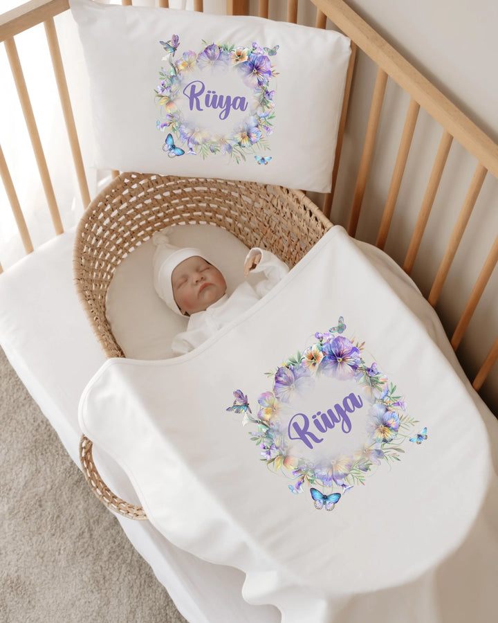 Gepersonaliseerde babydeken en kussen met bloemenprint en naam in een wieg voor newborn meisjes.