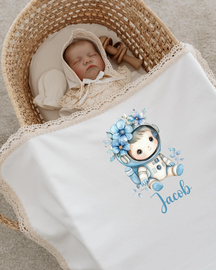 Newborn sleeping in a cozy basket, wrapped in a personalized astronaut blanket with name Jacob and floral details.