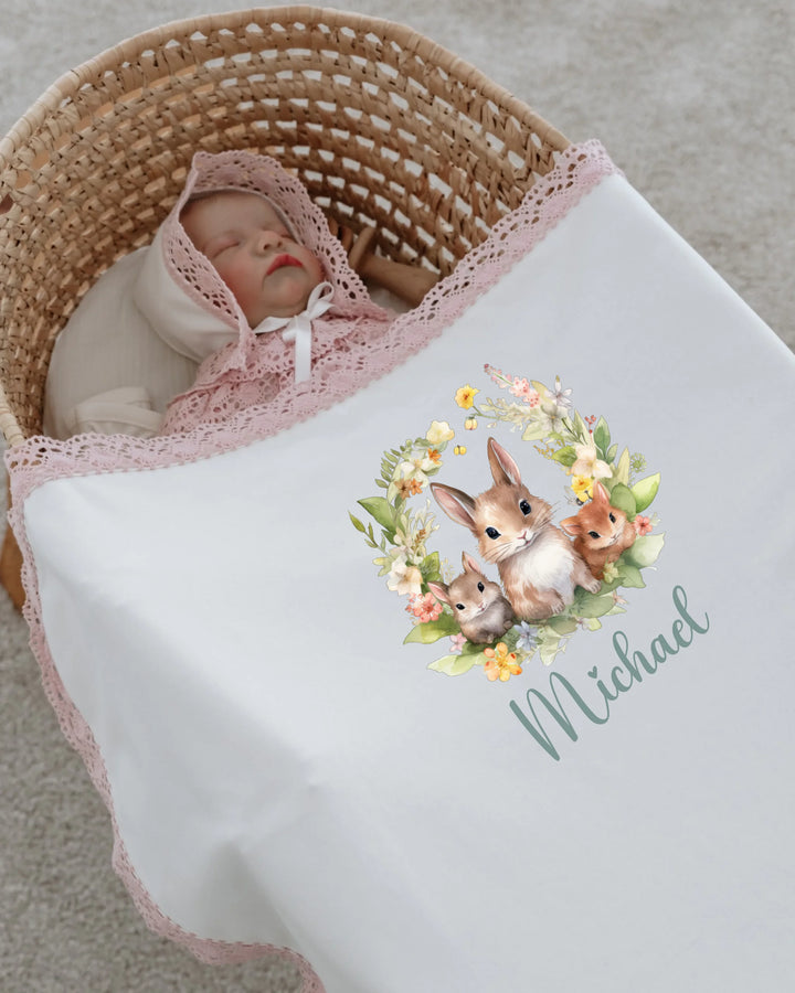 Newborn baby sleeping in a basket covered with a personalized blanket featuring cute forest animals and flowers.