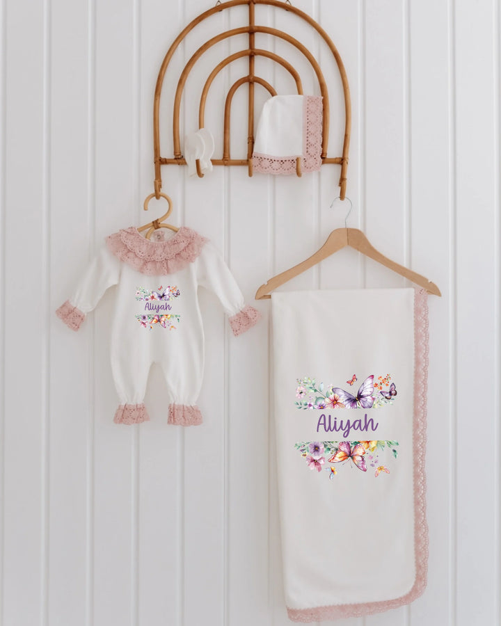 4-piece newborn girl clothing set with floral and butterfly design, including a romper, blanket, and hat in soft pastels.