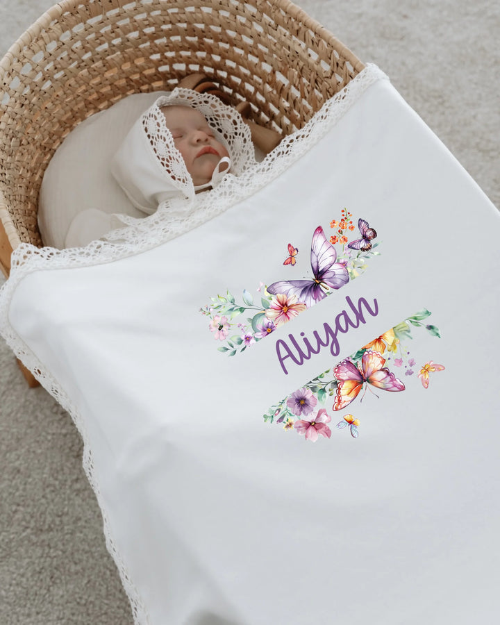 Newborn girl in a basket covered with a floral blanket featuring butterflies and the name Aliyah.