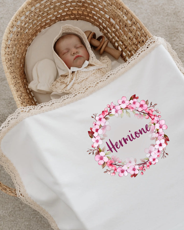 Newborn sleeping in a cozy basket with personalized floral blanket featuring the name 'Herrione'.