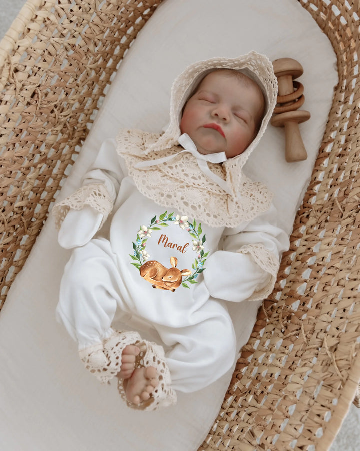 Slaapende baby in een romper met bloemenkrans, naam en kant, in een wiegje met natuurlijke uitstraling.