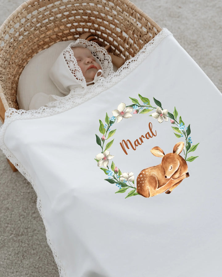 Newborn baby wrapped in a personalized blanket featuring a sleeping fawn and floral wreath design.