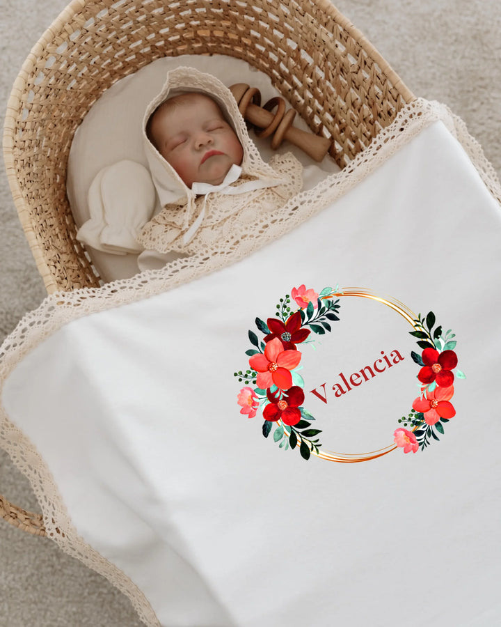 Newborn girl wrapped in a floral personalized blanket with the name 'Valencia' and elegant lace trim.