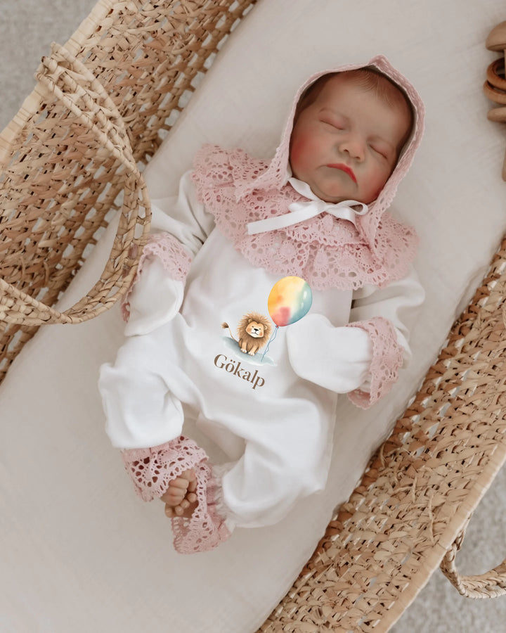 Adorable newborn girl in white outfit with lace, featuring balloon and lion design, perfect for a special gift.