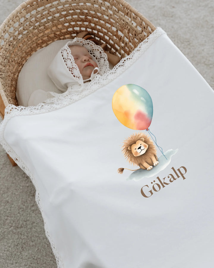 Newborn girl sleeping in a basket with a blanket featuring a lion holding a colorful balloon and the name 'Gökalp'.
