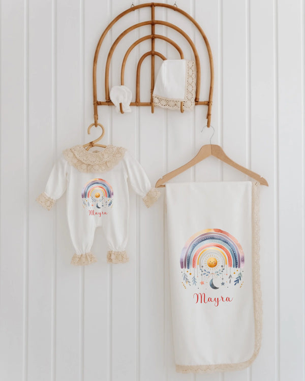 Newborn outfit set with rainbow design, personalized with the name Mayra, hanging on a decorative display.