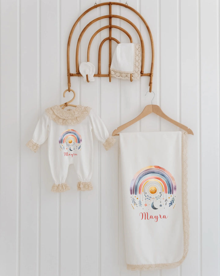 Newborn outfit set with rainbow design, personalized with the name Mayra, hanging on a decorative display.