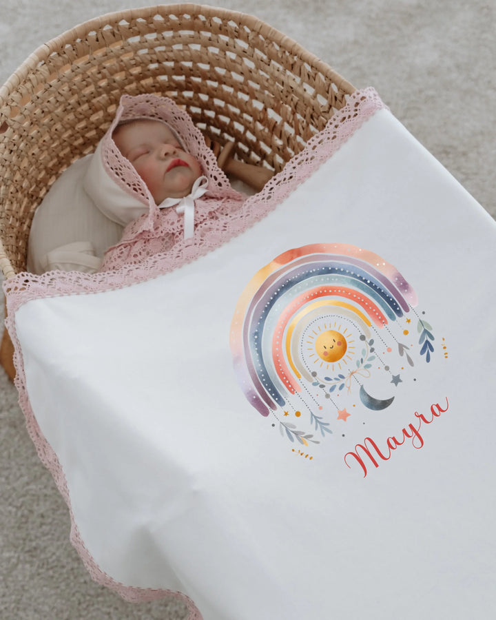 Newborn girl swaddled in a blanket with a colorful rainbow print and personalized name, Mayra, in a cozy basket.