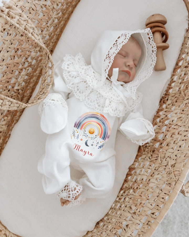 Newborn girl in colorful rainbow outfit with lace details, personalized with the name Mayra, in a cozy basket.