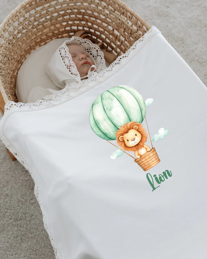 Baby sleeping under a white blanket with a lion in a hot air balloon design, showcasing a cute newborn outfit.