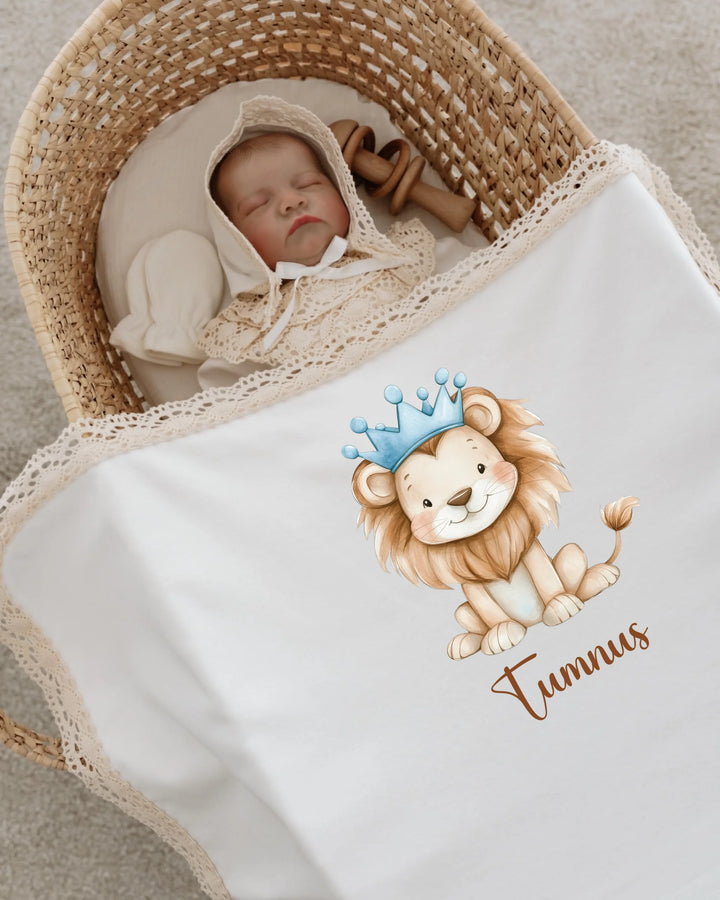 Newborn baby sleeping in a basket with a lion-themed blanket featuring name 'Tumnus' and lace trim.