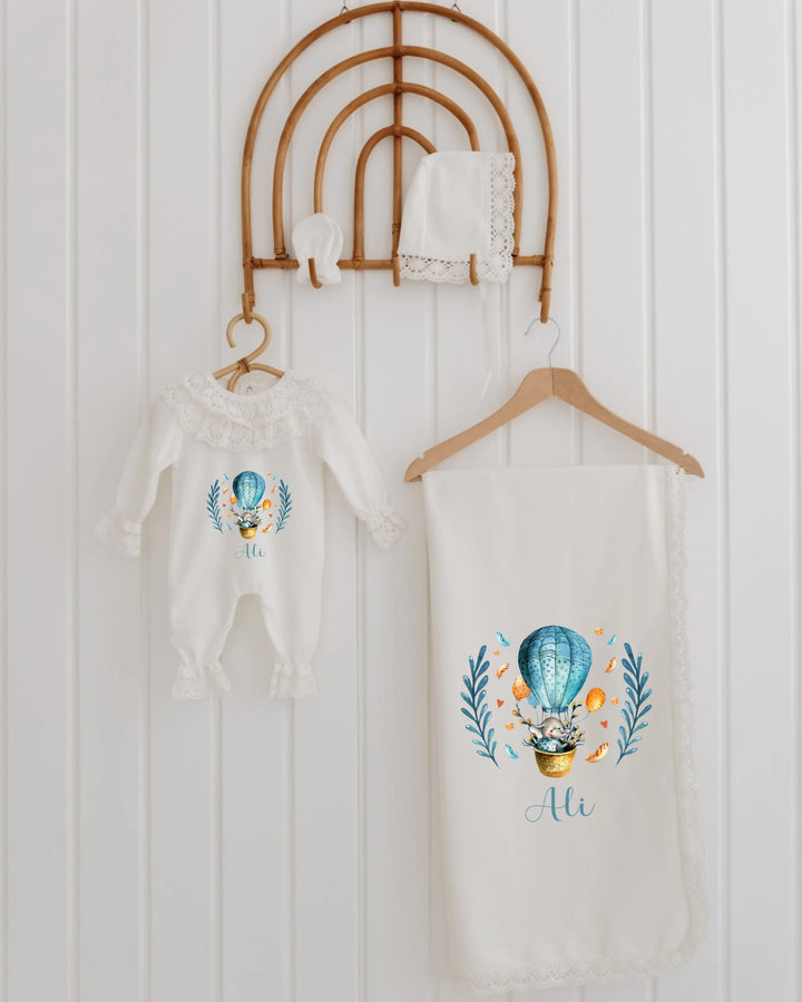 Luchtballon meisjes babykledingset met romper, mutsje en dekentje, gepersonaliseerd met naam en kleurrijke ballonprint.