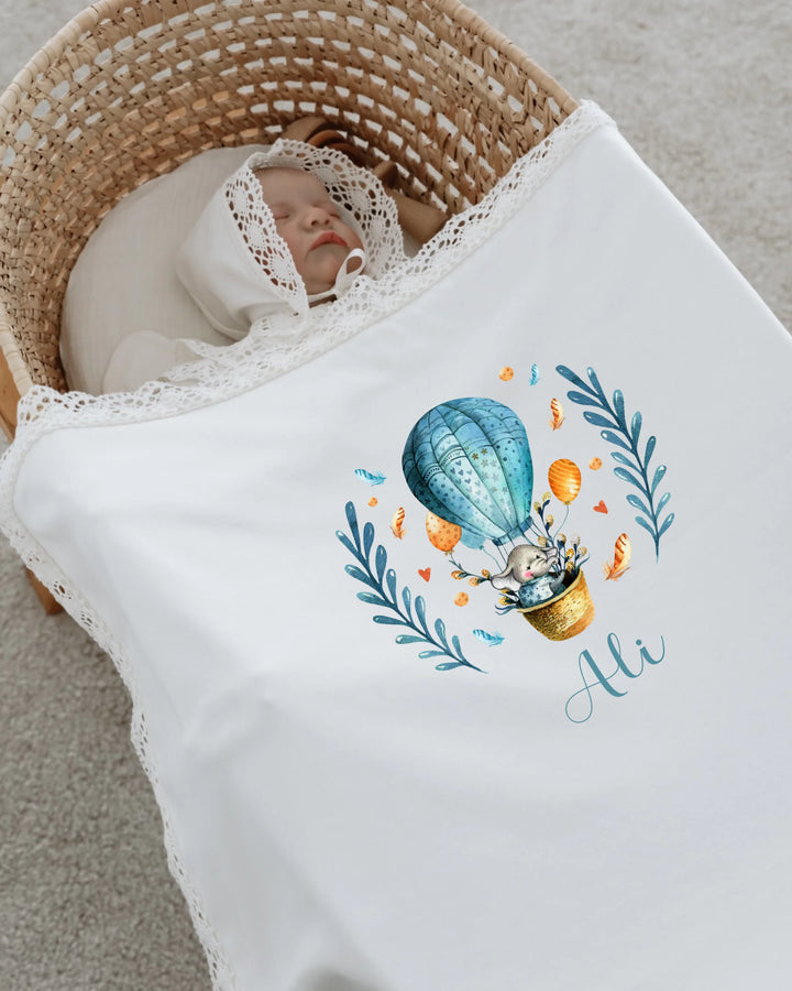 Schattige baby in een wieg, gewikkeld in een luchtballonprint dekentje met naam Ali.