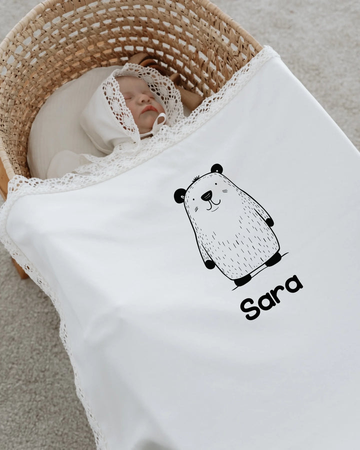 Newborn baby wrapped in a personalized bear blanket with lace, featuring the name Sara in a minimalist design.
