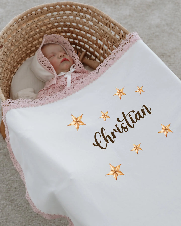 Baby nestled in a basket, wrapped in a personalized star-themed blanket with the name 'Christian'.