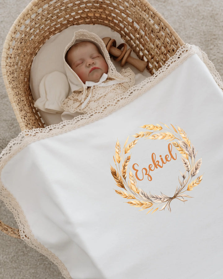 Newborn baby named Ezekiel sleeping in a cozy basket, wrapped in a personalized white blanket with lace.