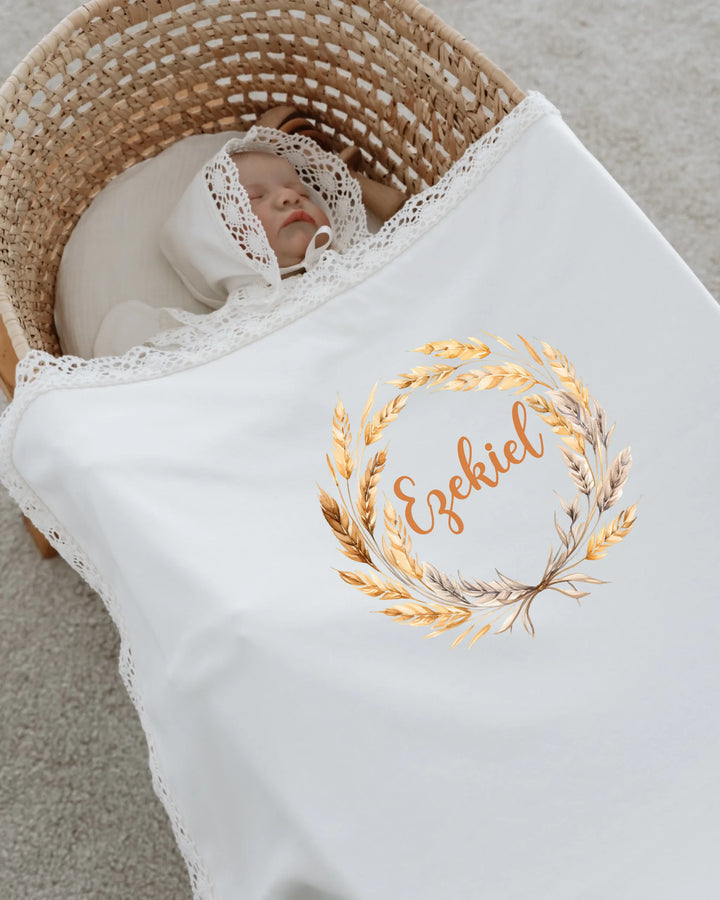 Pasgeboren baby gewikkeld in een witte deken met gouden illustratie in een rieten wieg.
