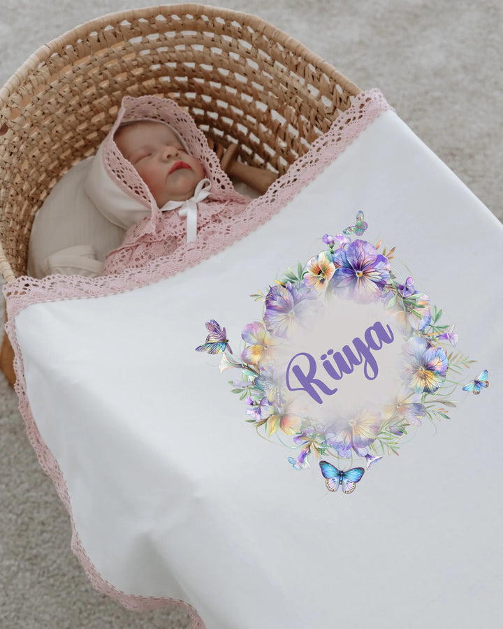 Newborn girl in a basket with a personalized floral blanket featuring the name Riya and delicate lace trim.