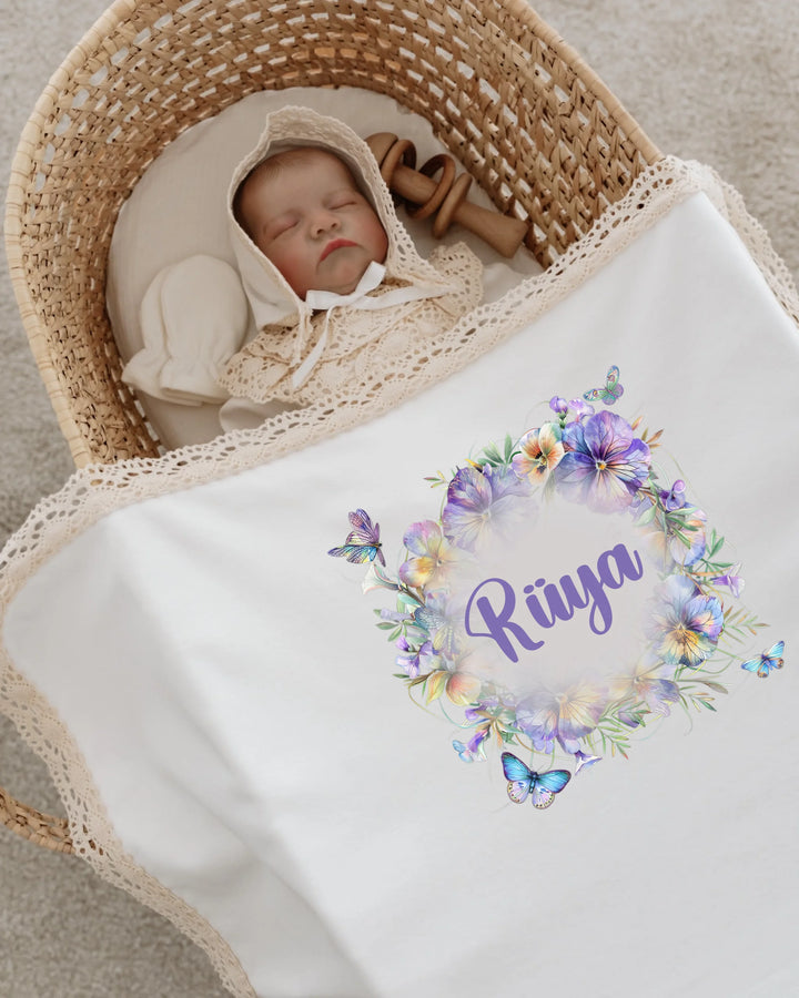 Newborn girl sleeping in a woven basket, covered with personalized floral blanket featuring the name Rüya.