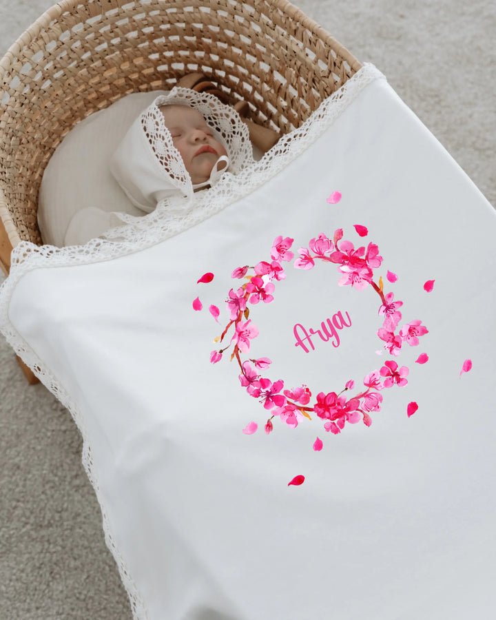 Newborn girl sleeping in a basket, wrapped in a personalized floral blanket with name Arya.