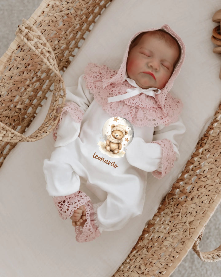 Newborn girl clothing set with lace details, featuring a teddy bear print in a cozy baby cradle.