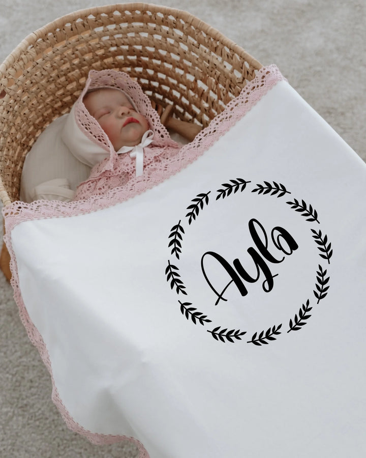 Newborn baby girl Ayla resting in a cozy basket wrapped in a personalized blanket with lace details.