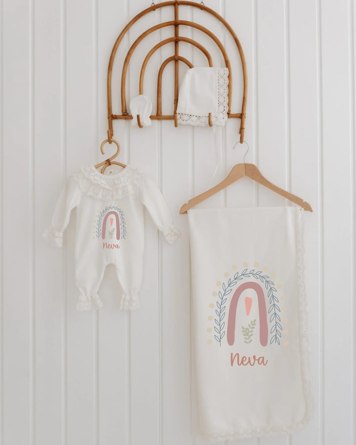 Pastel meisjes geboortepakje met regenboogillustratie, mutsje en dekentje, gepersonaliseerd met naam Neva.