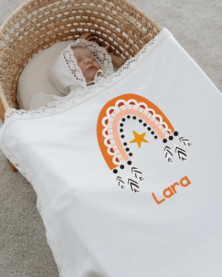 Geboren meisje ingepakt in gepersonaliseerd dekentje met boho regenboog en sterdetails.