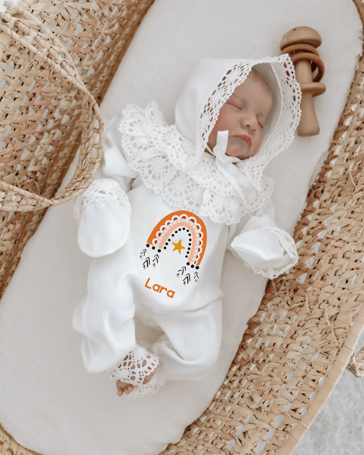 Newborn girl in bohemian rainbow romper with lace, personalized with name Lara, resting in a cozy bassinet.