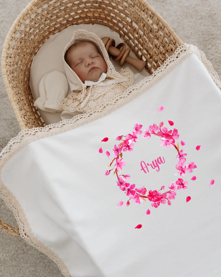 Newborn baby sleeping in a bassinet with personalized floral blanket featuring name 'Arya'.