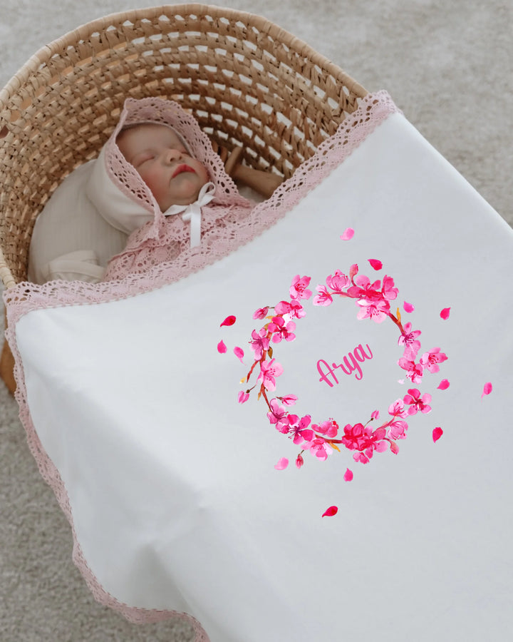 Newborn girl sleeping in a cozy basket, wrapped in a personalized blanket with a pink floral design and the name 'Arya'.