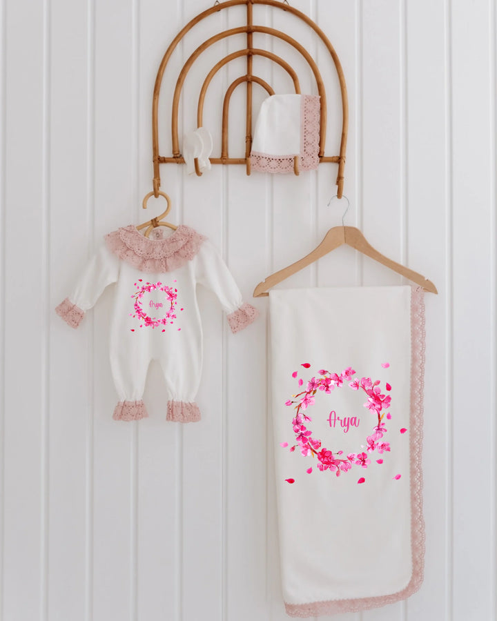 Roze geboortepakje met kant en bloemenprint voor meisjes, gepersonaliseerd met naam en bijpassende dekentje.
