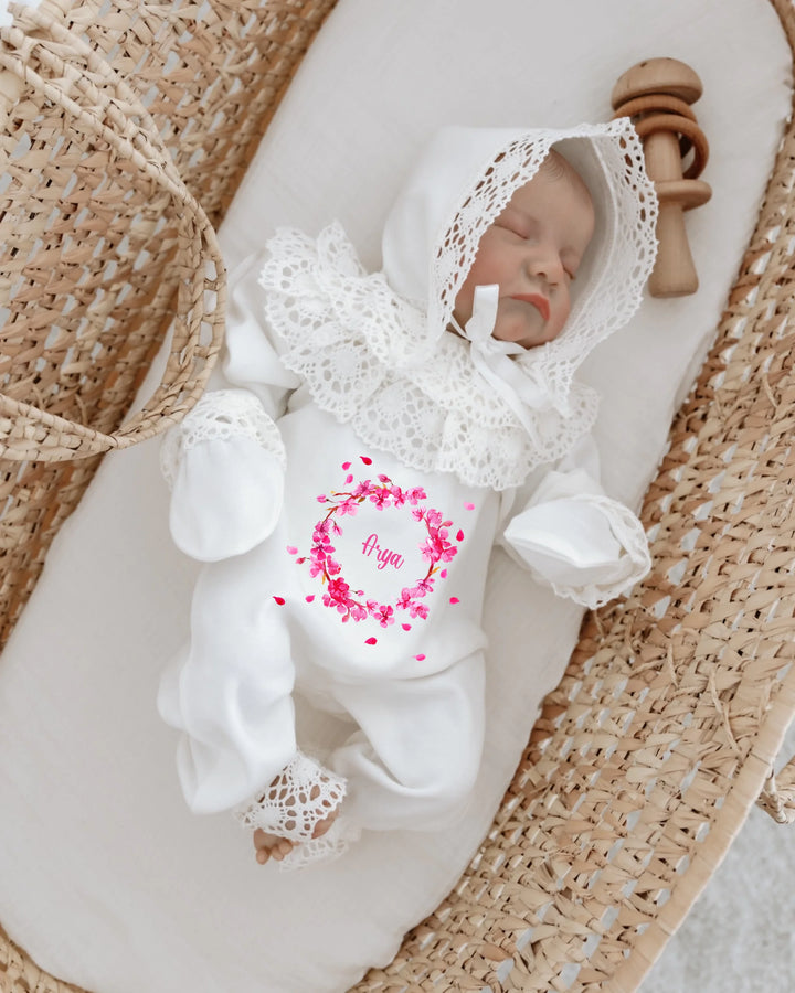 Newborn girl in personalized white outfit with lace and pink floral print, sleeping in a basket.
