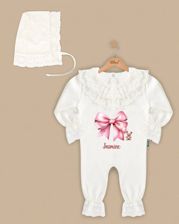 Elegante witte kanten babypakje met roze strik en naam, compleet met bijpassend mutsje.