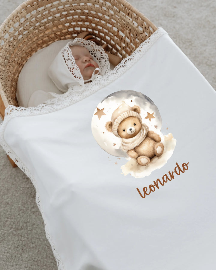 Newborn baby sleeping in a basket, covered with a blanket featuring a teddy bear design and the name 'Leonardo'.