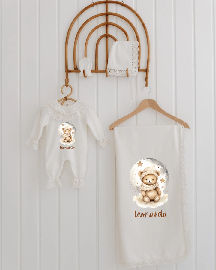 Newborn baby set with teddy bear print, personalized blanket, and matching outfit hanging decoratively.